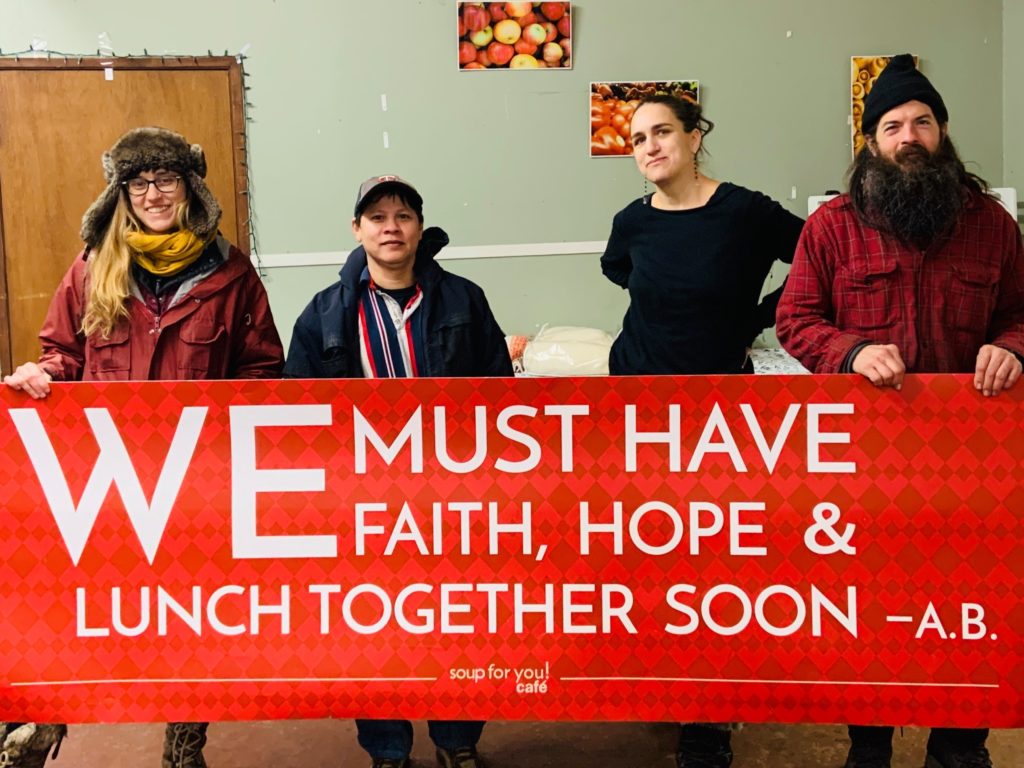 People holding a banner that reads We must have faith, hope and lunch together soon - A.B.