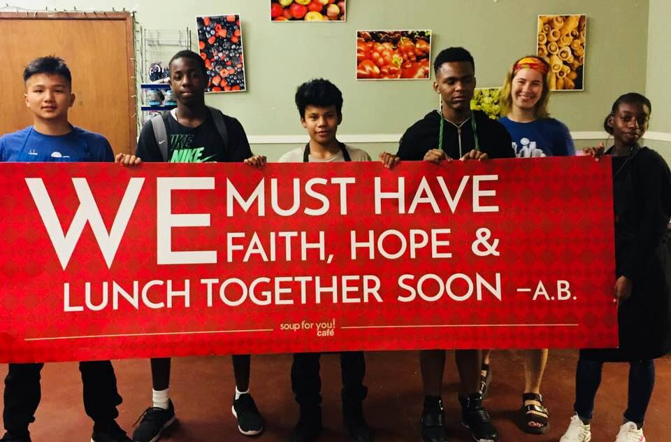 People holding a banner that reads We must have faith, hope and lunch together soon - A.B.