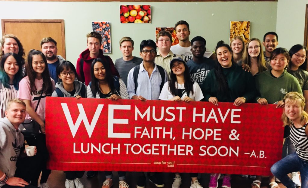 People holding a banner that reads We must have faith, hope and lunch together soon - A.B.