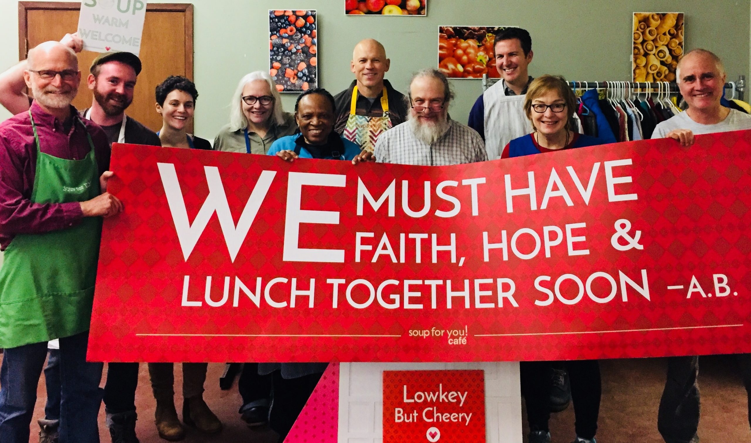People holding a banner that reads We must have faith, hope and lunch together soon - A.B.