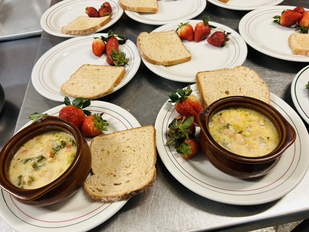 Plates with bread, strawberries and bowls of soup